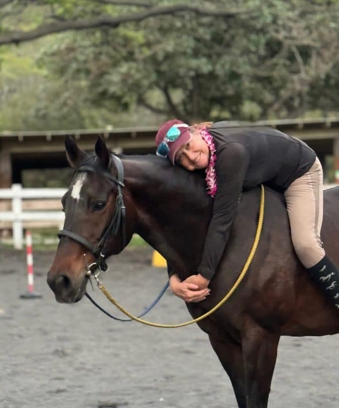 Kim Hollandsworth of Aloha Riding Lessons hugging her bay horse